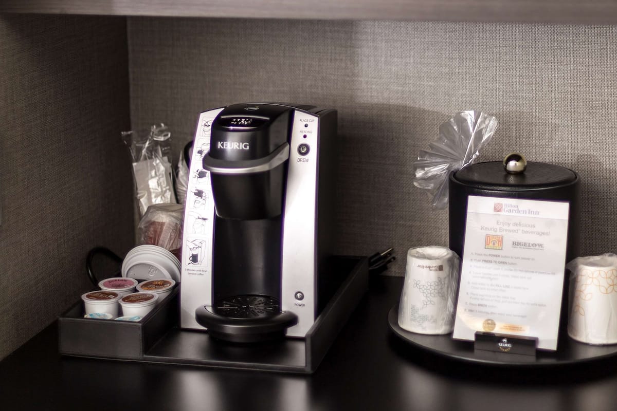 A microwave above a coffee maker on a countertop, with a menu card and coffee pods below.