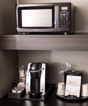 A microwave above a coffee maker on a countertop, with a menu card and coffee pods below.