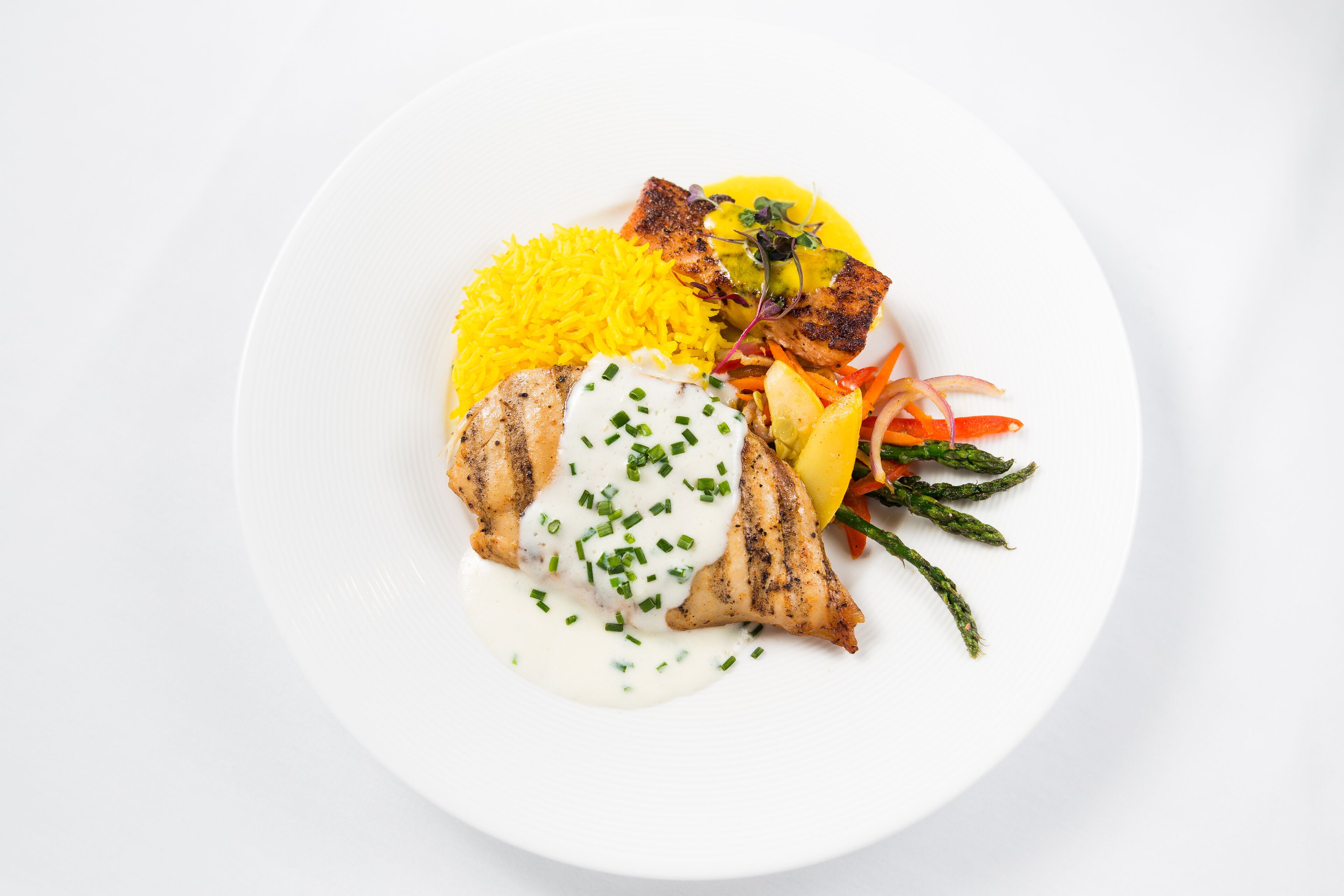 Un plato blanco con pollo a la parrilla, arroz amarillo y una guarnición de verduras.