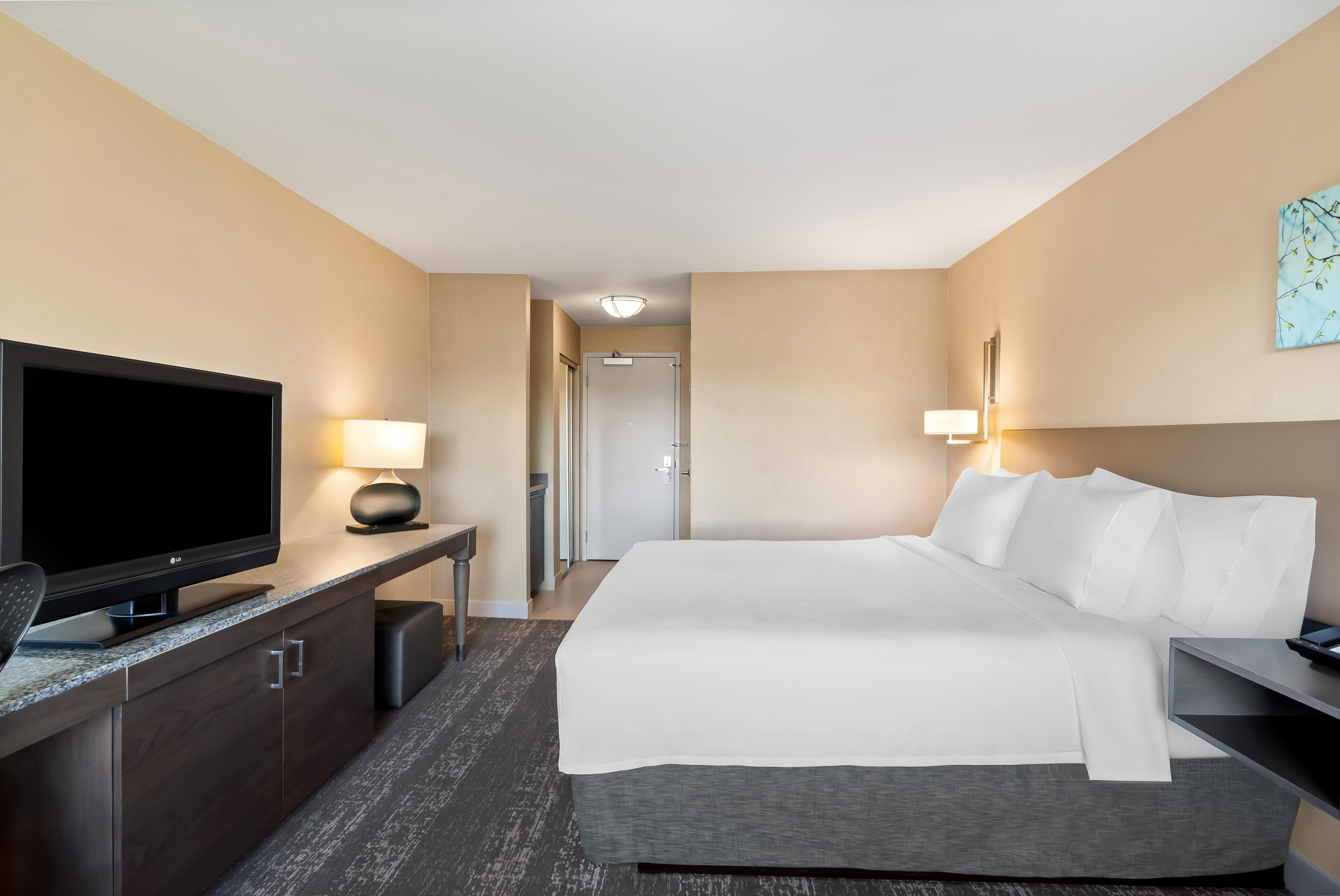A hotel room with a bed, a TV, a desk, and a lamp.