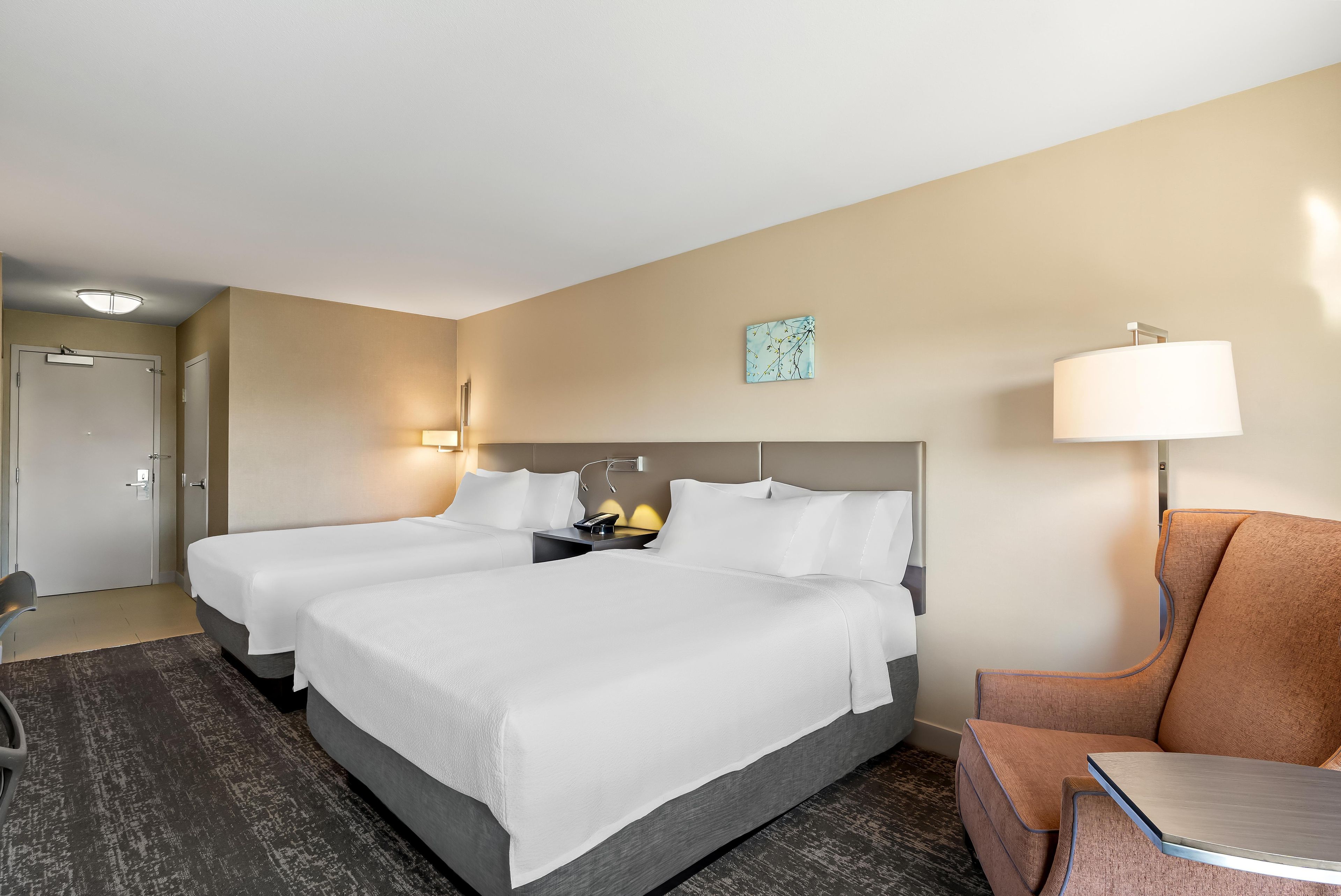Habitación de hotel con dos camas, un escritorio, una silla y una lámpara de pared.