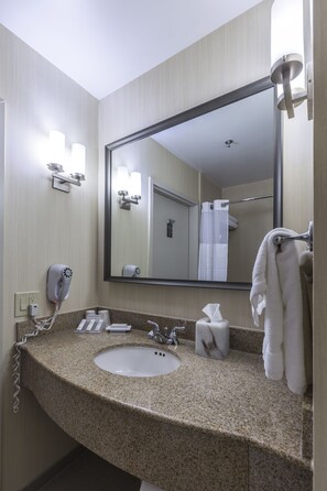Un bany d'hotel amb un lavabo de superfície de granit, un mirall gran, un escurapulides i un assecador de mans.