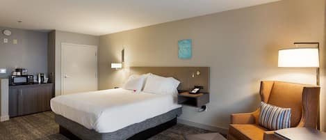 Quarto de hotel com uma cama grande, uma escrivaninha, uma cadeira e uma mesinha.