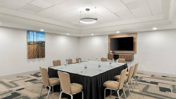 Un salón de conferencias con una gran mesa, sillas, un televisor de pantalla plana y un cuadro en la pared.