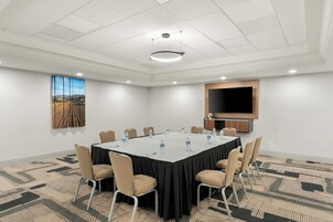 Un salón de conferencias con una gran mesa, sillas, un televisor de pantalla plana y un cuadro en la pared.