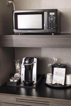 Una estación de café con una cafetera Keurig, un microondas y una bandeja con cápsulas de café y un menú.
