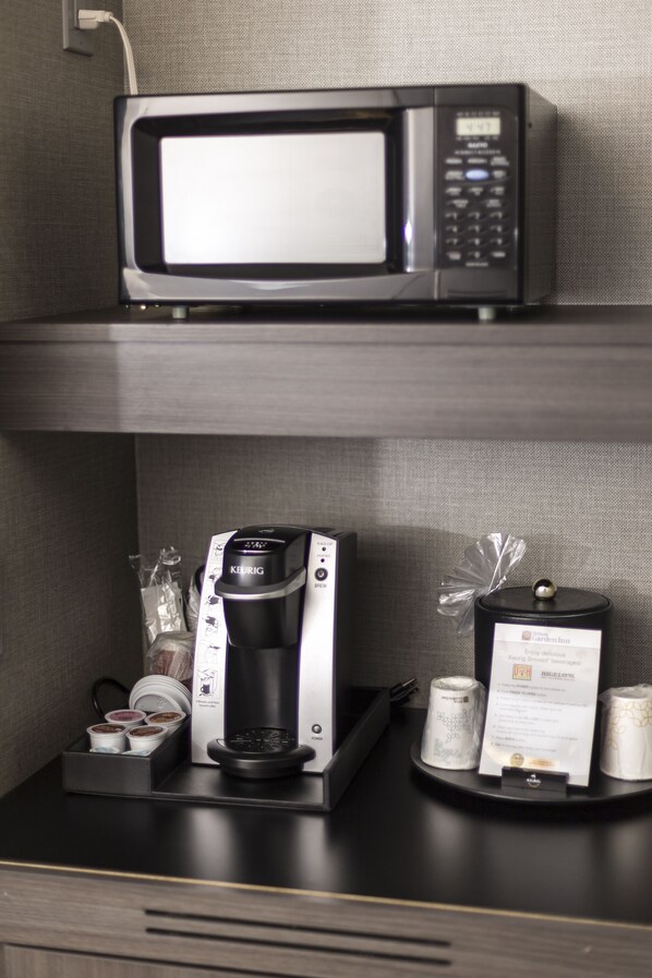 Una estació de cafè amb una màquina de cafè Keurig, un microones i una safata amb càpsules de cafè i un menú.