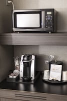 Una estación de café con una cafetera Keurig, un microondas y una bandeja con cápsulas de café y un menú.