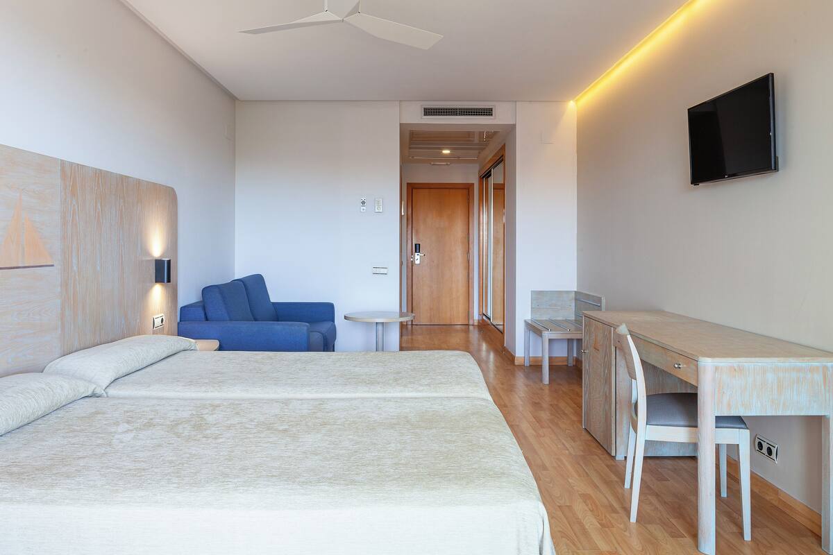Ein Hotelzimmer mit zwei Betten, einem Schreibtisch, einem Stuhl, einem Fernseher und einem Sofa.