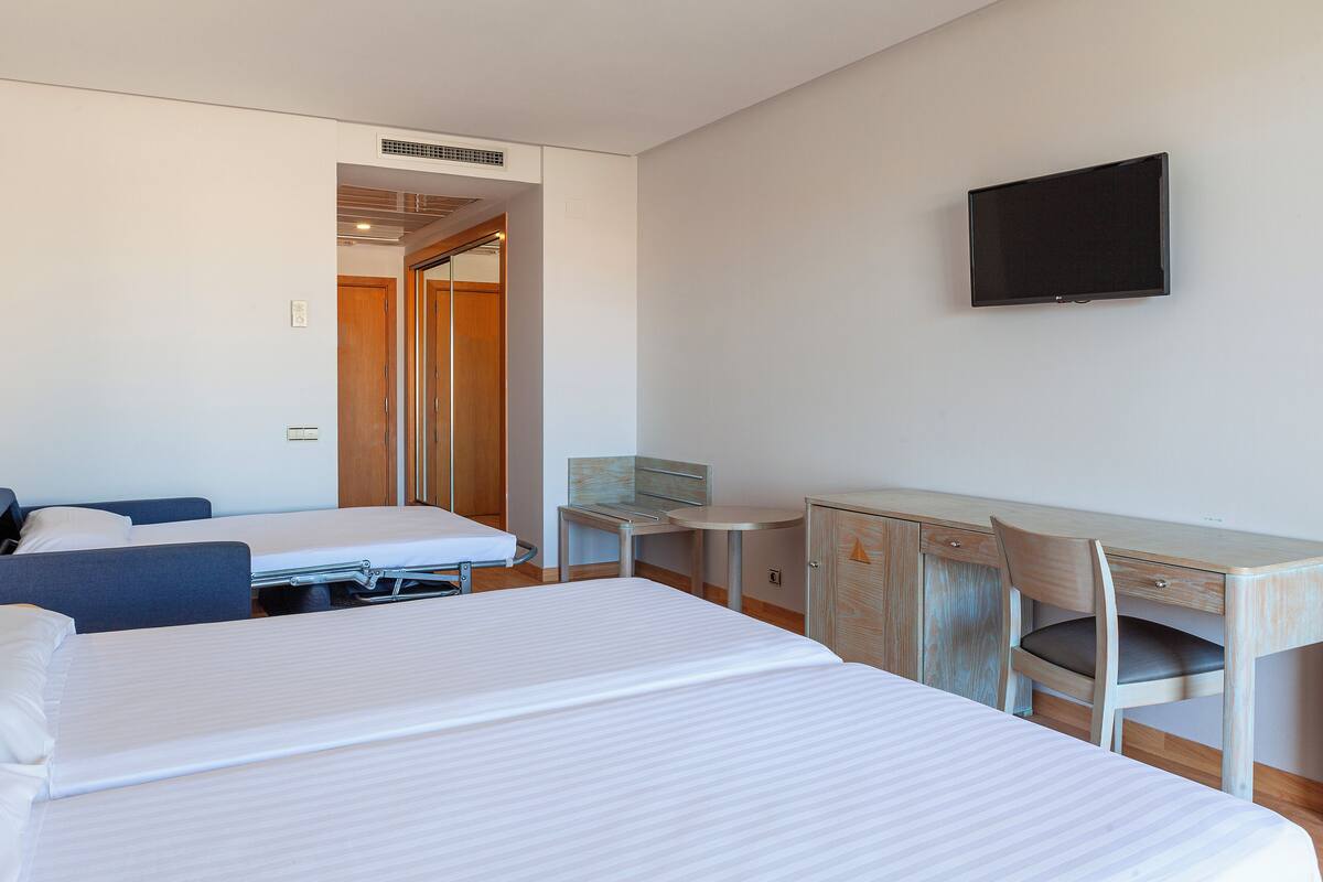 Ein Hotelzimmer mit zwei Betten, einem Schreibtisch, einem Sessel und einem Fernseher.