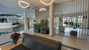 Un área de recepción moderna con un mostrador, asientos, plantas en macetas y vistas al exterior.
