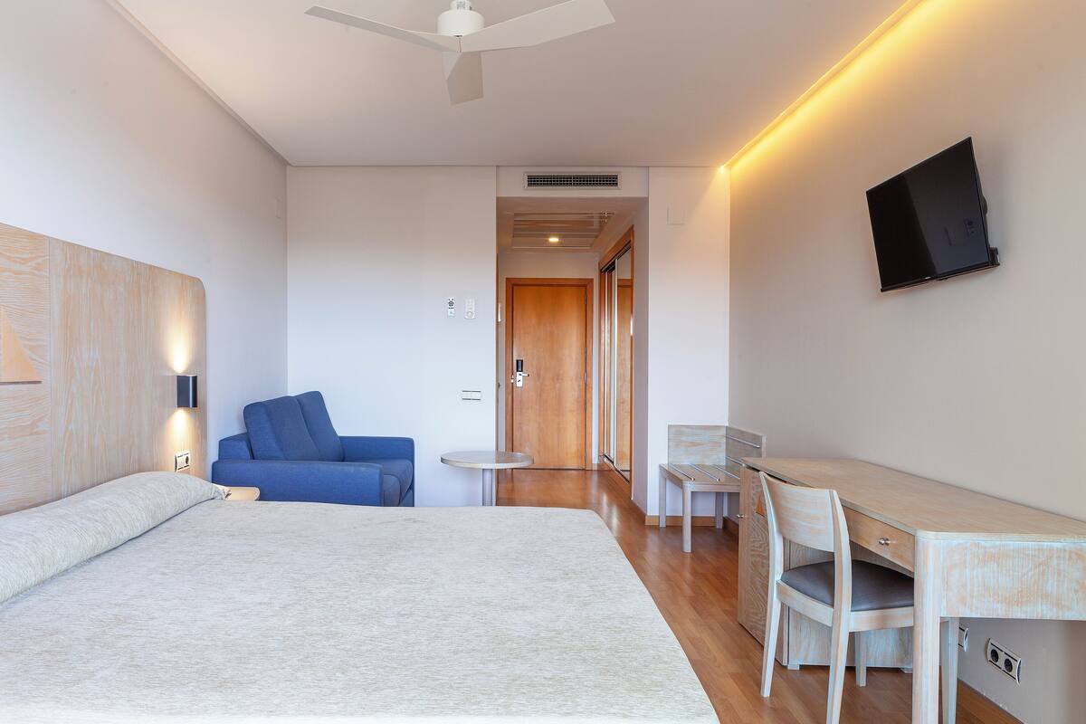 Ein modernes Hotelzimmer mit einem großen Bett, einem Schreibtisch, einem Stuhl, einem blauen Sofa und einem flachbildfernseher an der Wand.