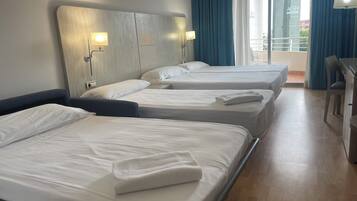A hotel room with three single beds, a desk, and a chair.
