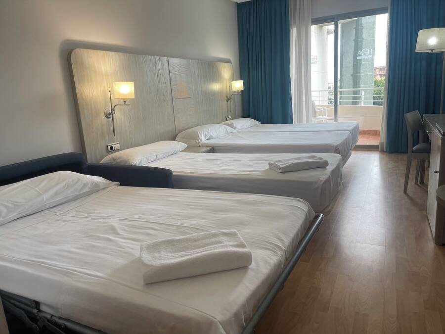 A hotel room with three single beds, a desk, and a chair.