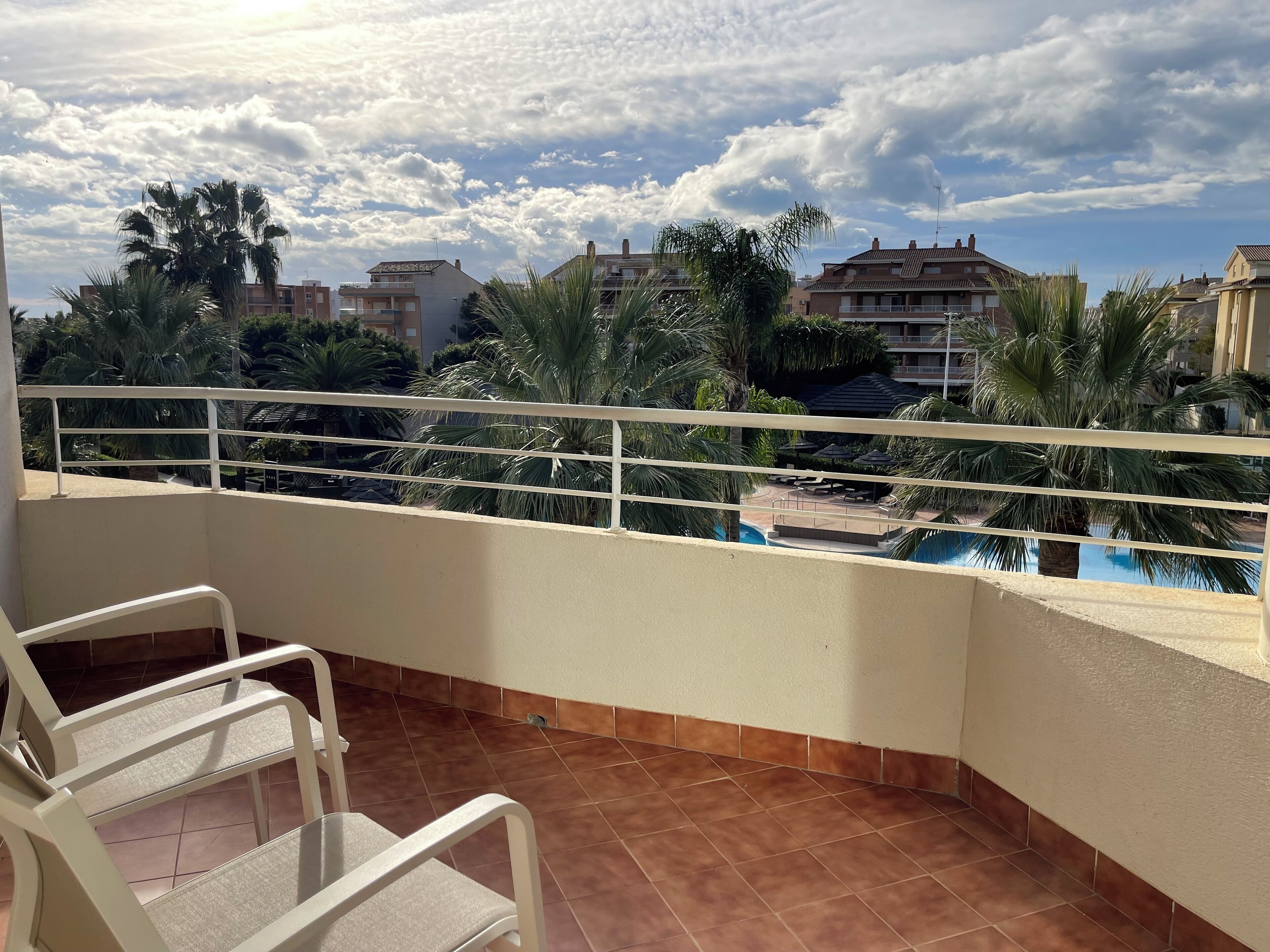 Un balcón con vistas a una piscina, rodeado de palmeras y edificios residenciales.