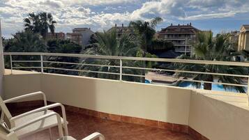 Un balcón con vistas a una piscina, rodeado de palmeras y edificios residenciales.