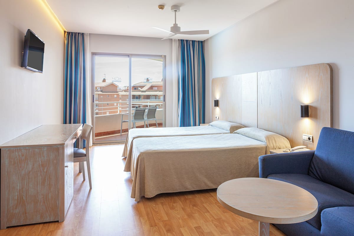Ein Hotelzimmer mit Bett, Schreibtisch, Stuhl, Sofa und einem Balkon mit Blick auf Gebäude.