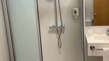 Un baño moderno con ducha envuelta en vidrio, un lavabo blanco con dispensador de jabón y una puerta de madera.
