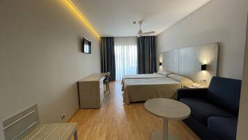 Habitación de hotel con escritorio, dos camas, sofá, una mesita y ventilador de techo.