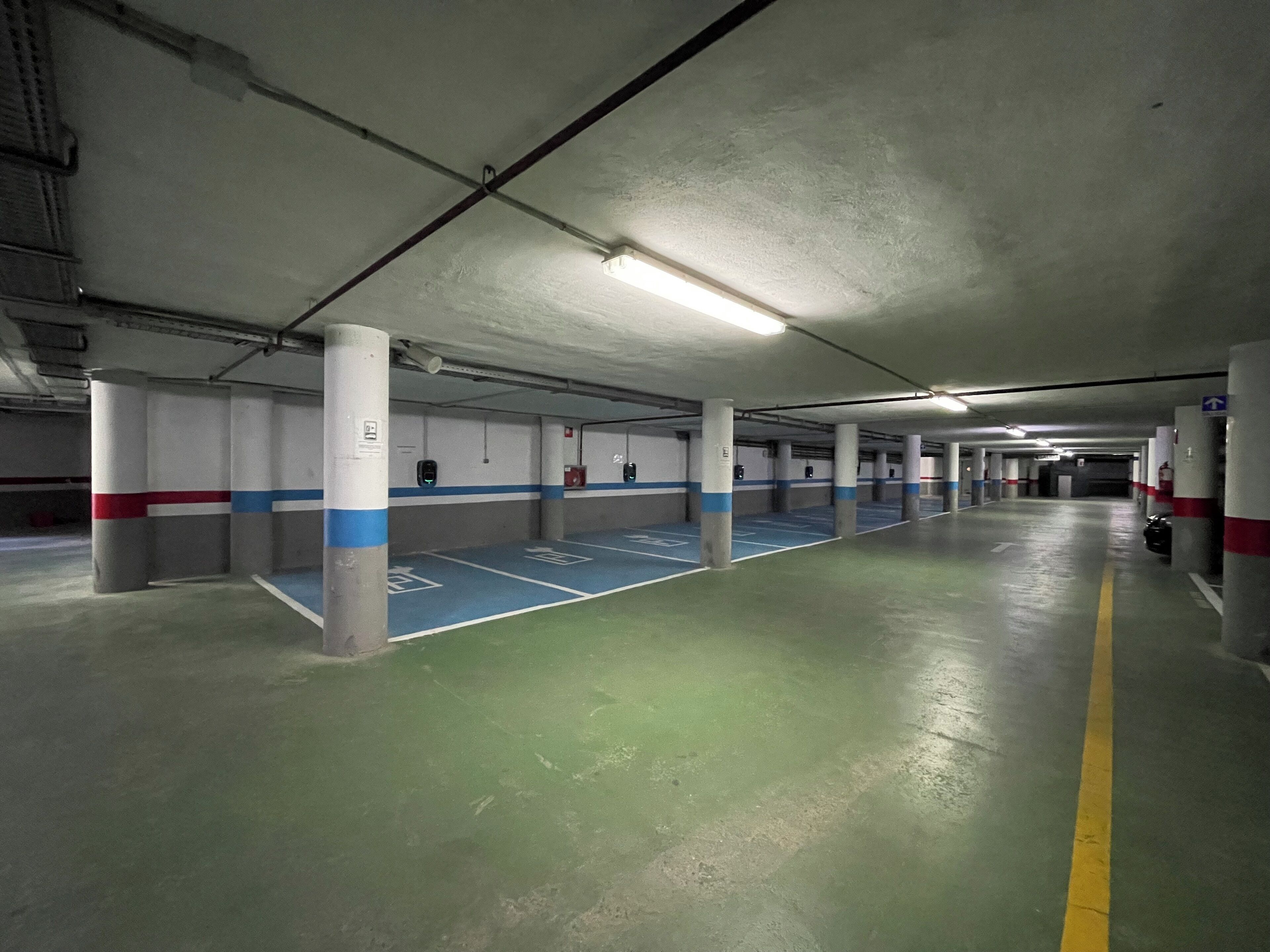 A multi-level parking garage with concrete pillars, blue parking spaces, and a green floor.