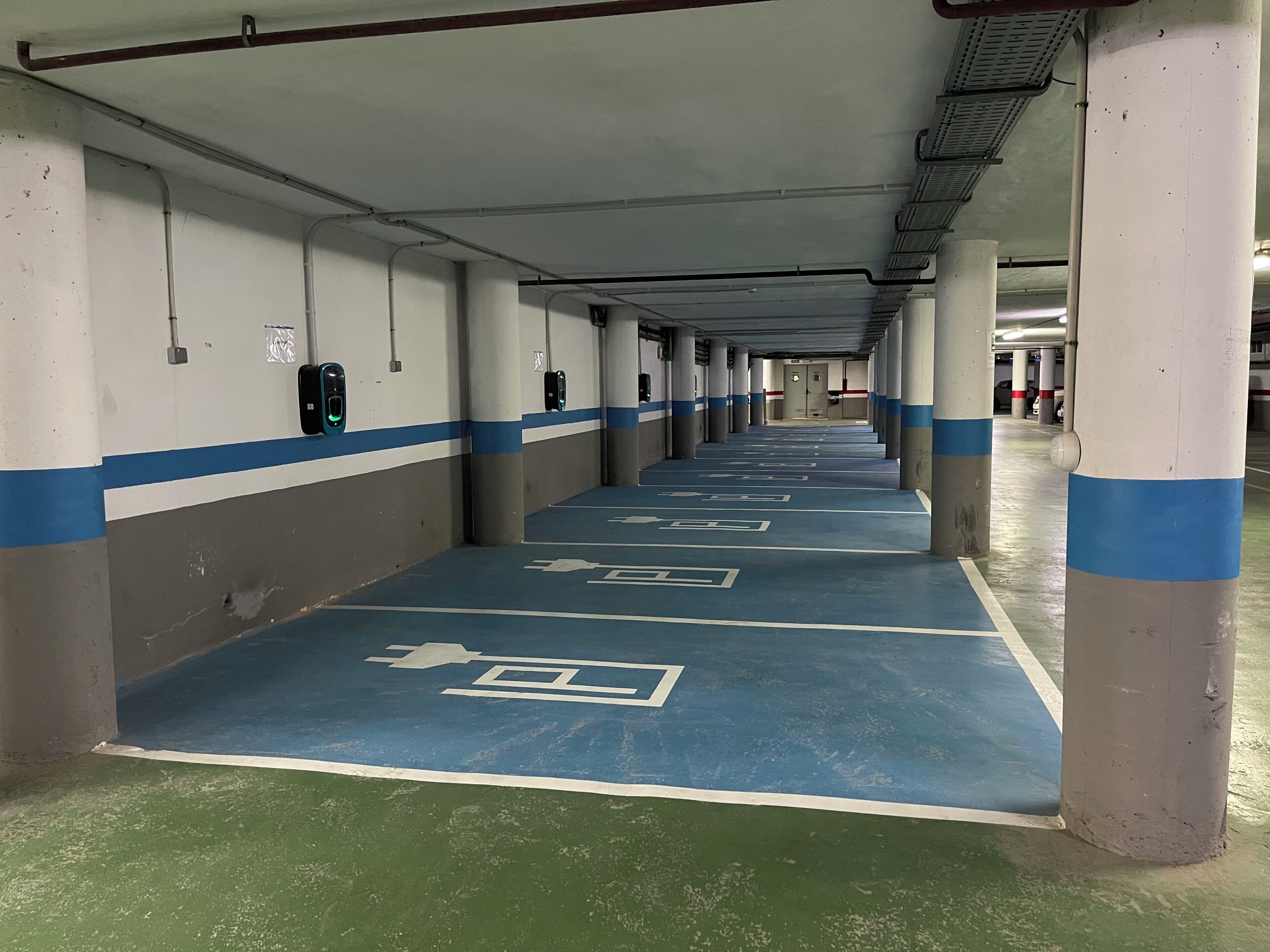 Un long parking souterrain, vide, avec des voies, des piliers peints en bleu et en blanc, et un sol vert.