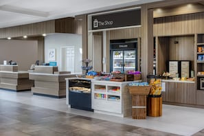 Un vestíbulo de hotel con mostrador de recepción, exhibición de bebidas frías y una sección de recuerdos locales.