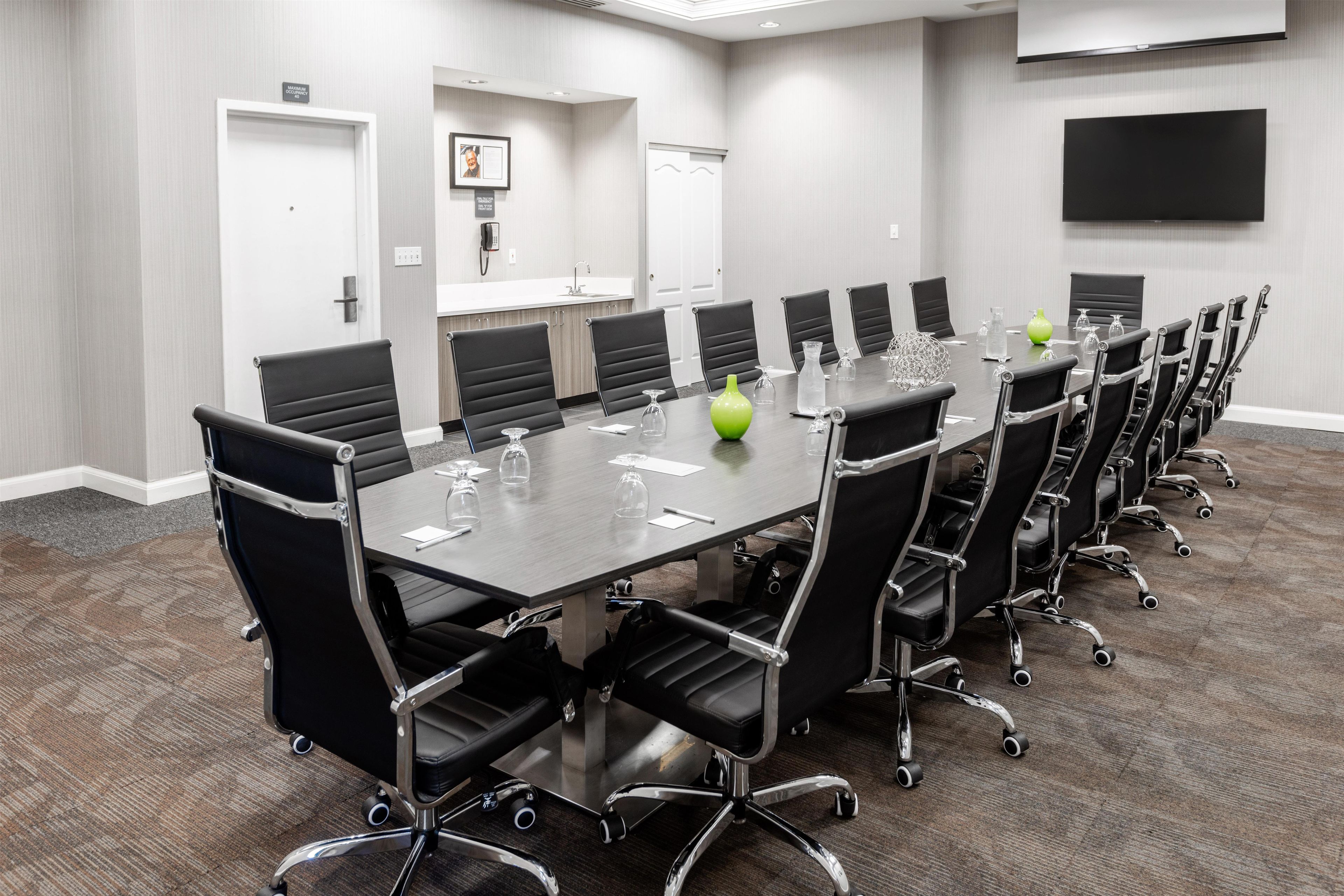 A conference room with a long table, black chairs, and a flat-screen TV on the wall.