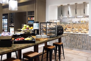 Un buffet de petit-déjeuner proposant une variété d’aliments, notamment des fruits, des viennoiseries et des boissons, dans un cadre d’hôtel moderne.