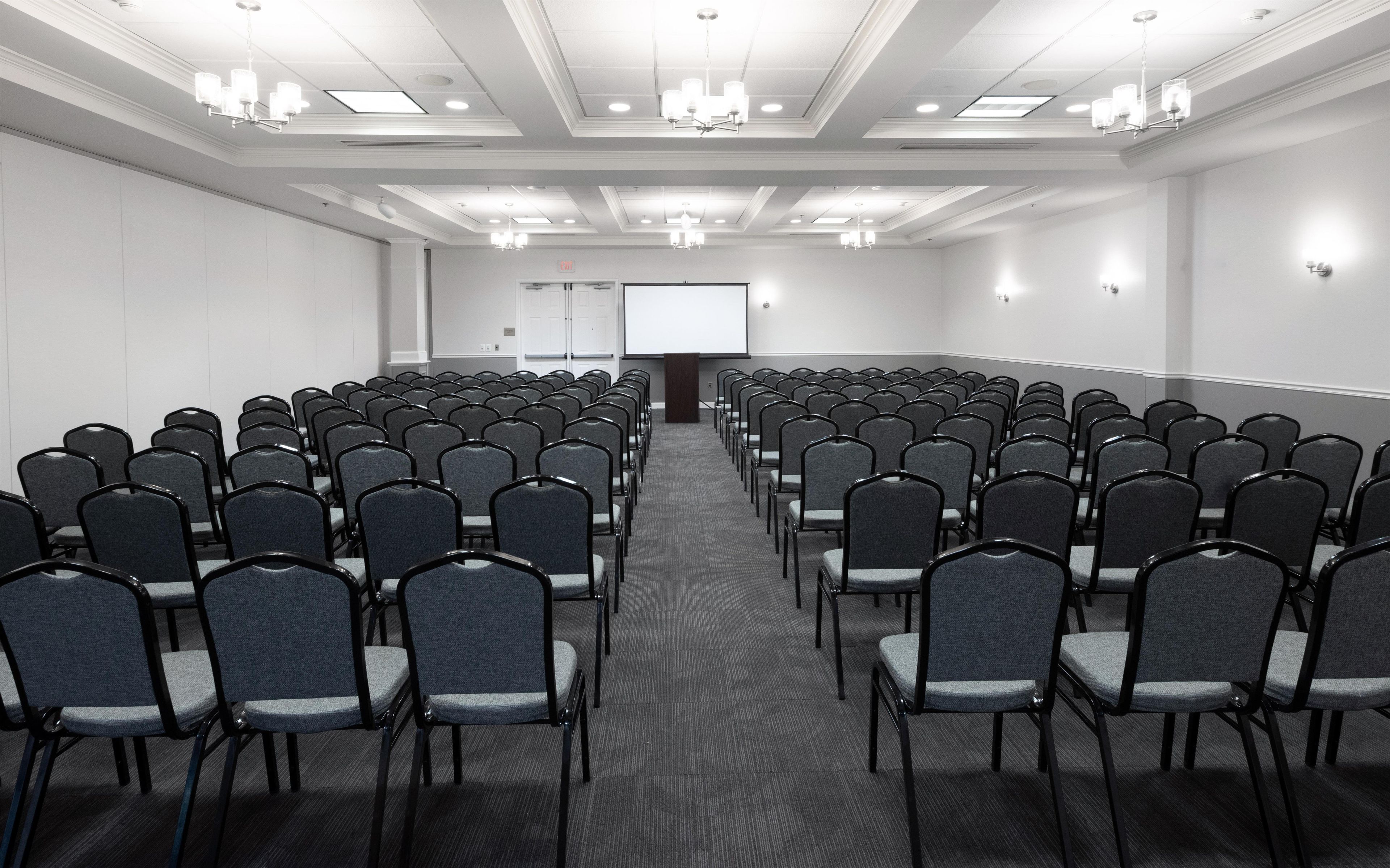 A conference room with rows of chairs, a projector screen, and a podium.