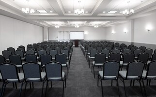 Un salón de conferencias con filas de sillas, una pantalla para proyector y un atril.