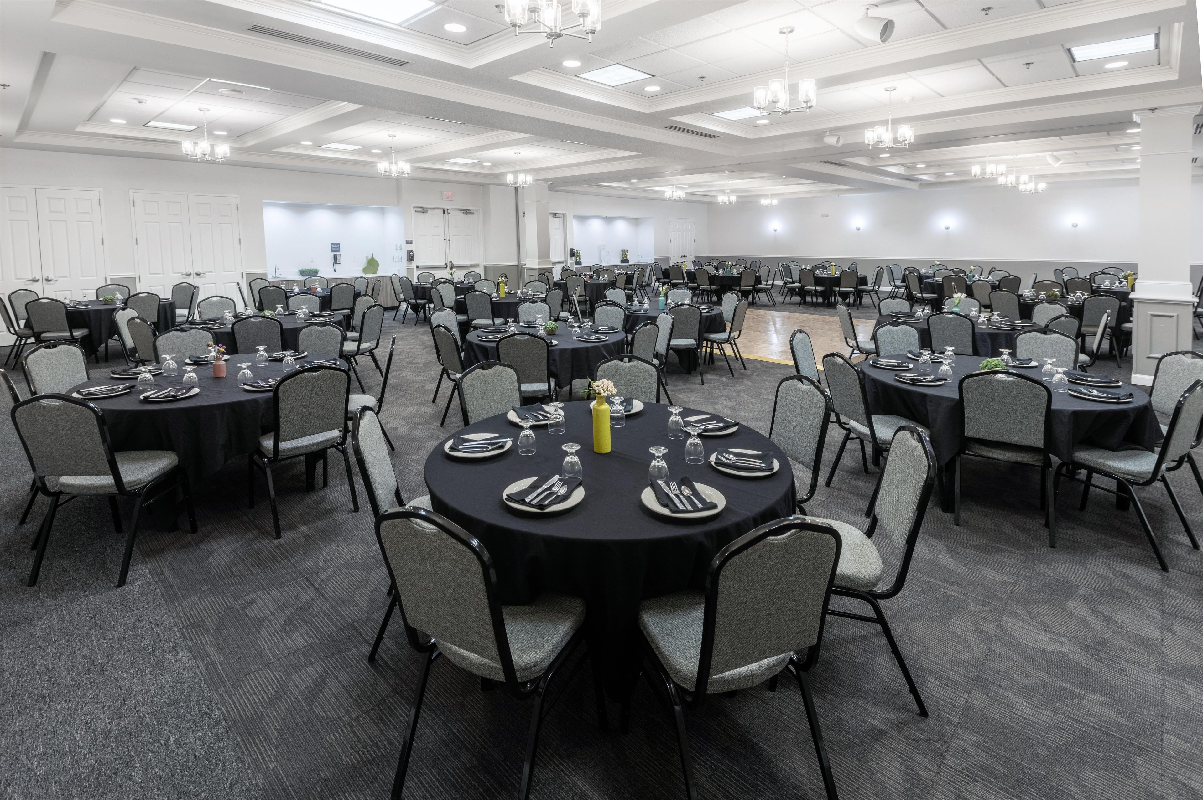 A large conference room with multiple round tables, each set with plates, cutlery, and glasses.