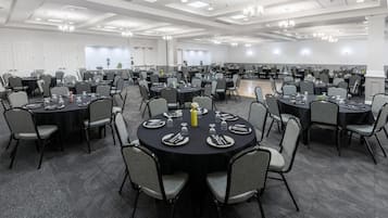 A large conference room with multiple round tables, each set with plates, cutlery, and glasses.