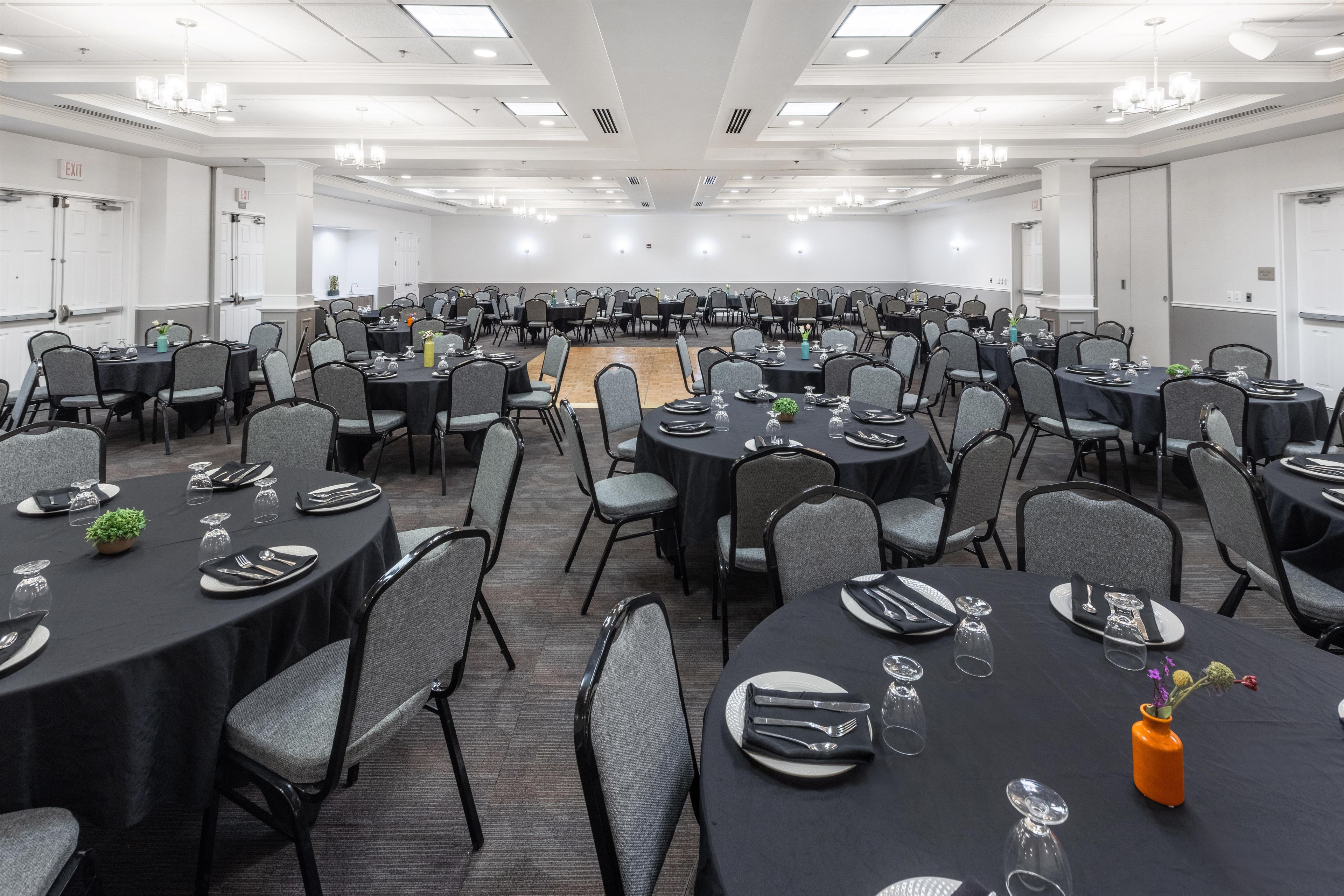 A large conference room with multiple tables set for dining, equipped with chairs and table settings.