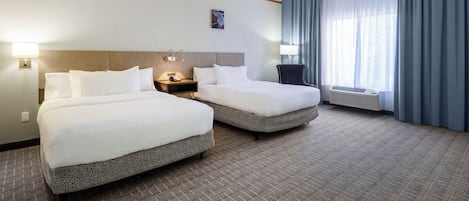 A hotel room with two beds, a nightstand, a lamp, a window with curtains, and an air conditioning unit.