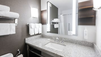 A modern bathroom with a granite countertop, a white sink, a large mirror, and a towel rack with folded towels.