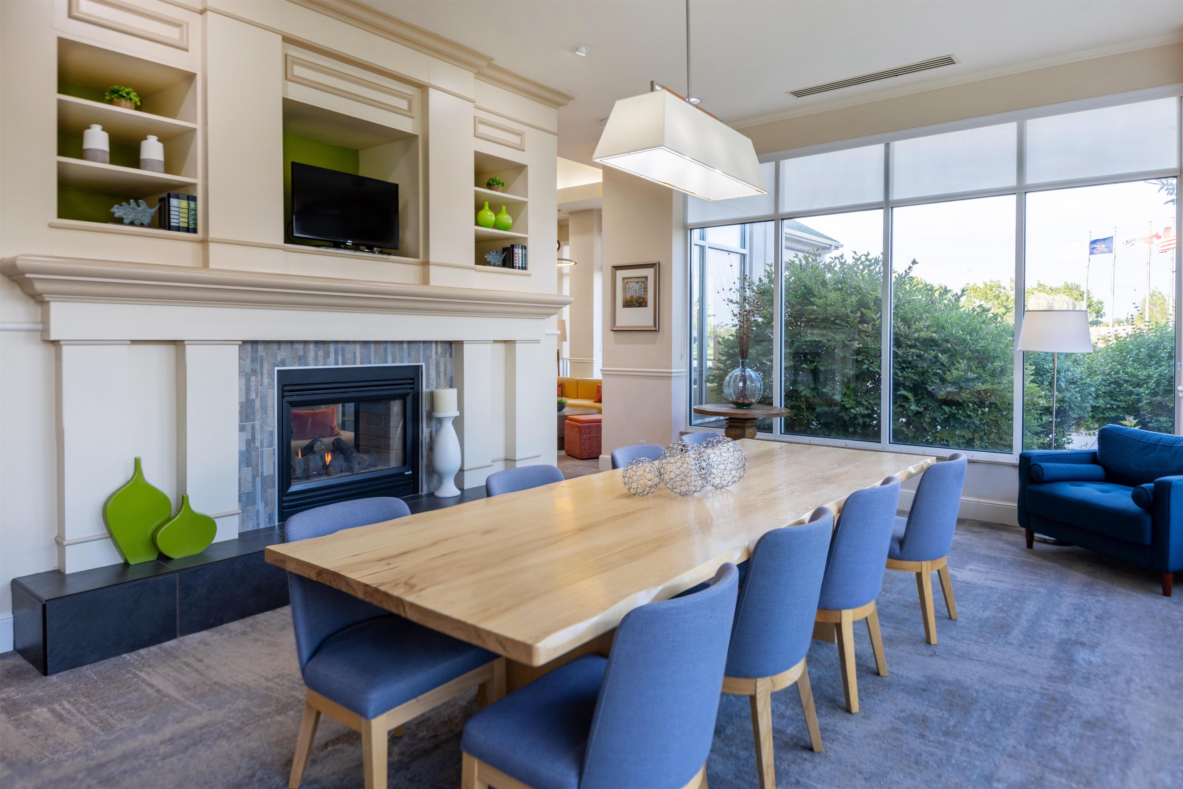 A modern dining area with a fireplace, a large wooden table, and blue chairs.