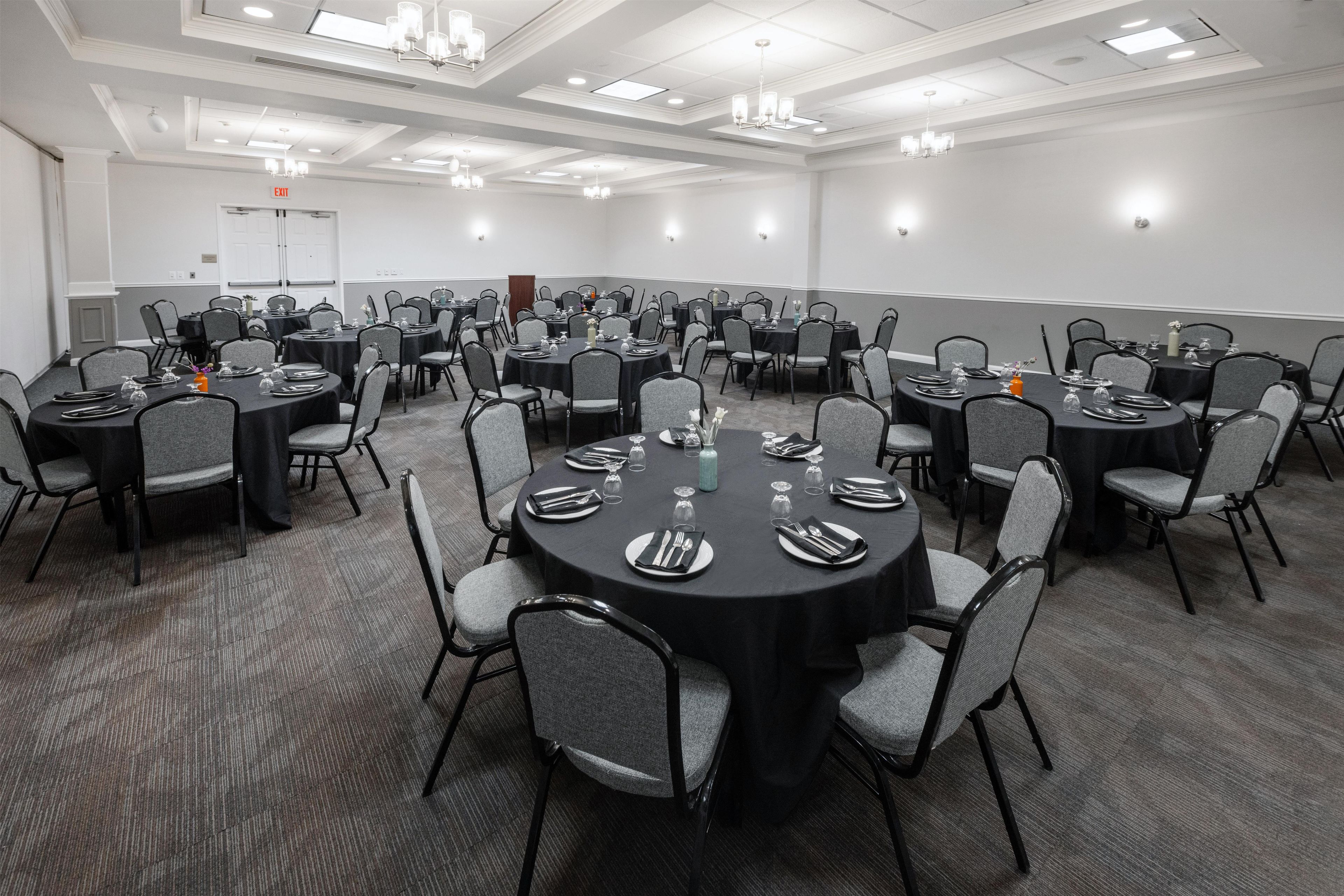 A conference room with round tables, grey chairs, and black tablecloths.