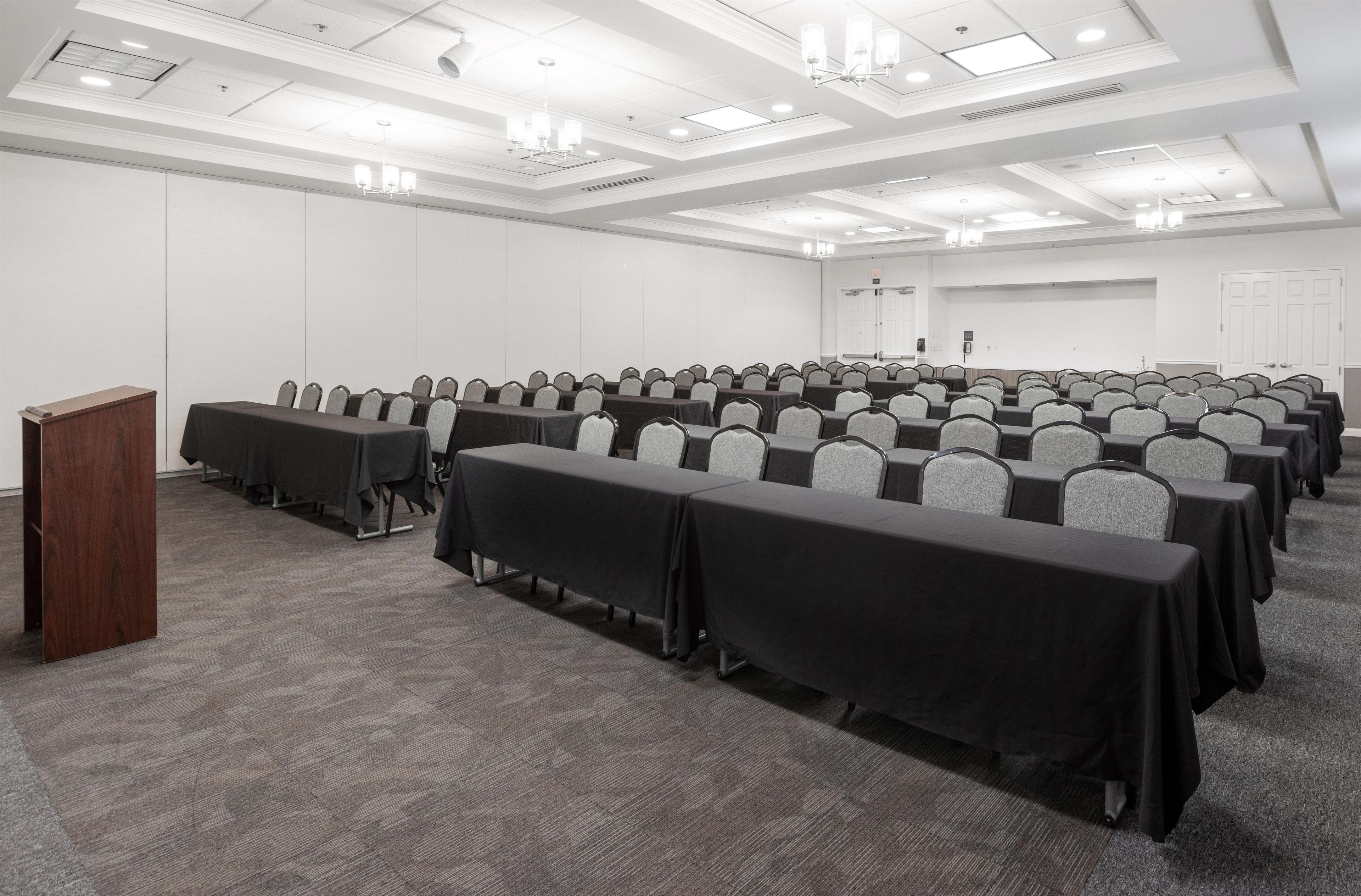 A conference room with rows of tables and chairs, a podium, and a door in the background.