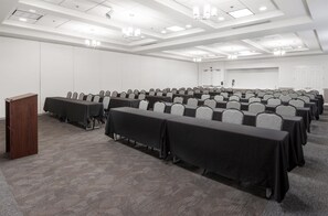 A conference room with rows of tables and chairs, a podium, and a door in the background. - Hilton Garden Inn Grand Forks - UND (Grand Forks)