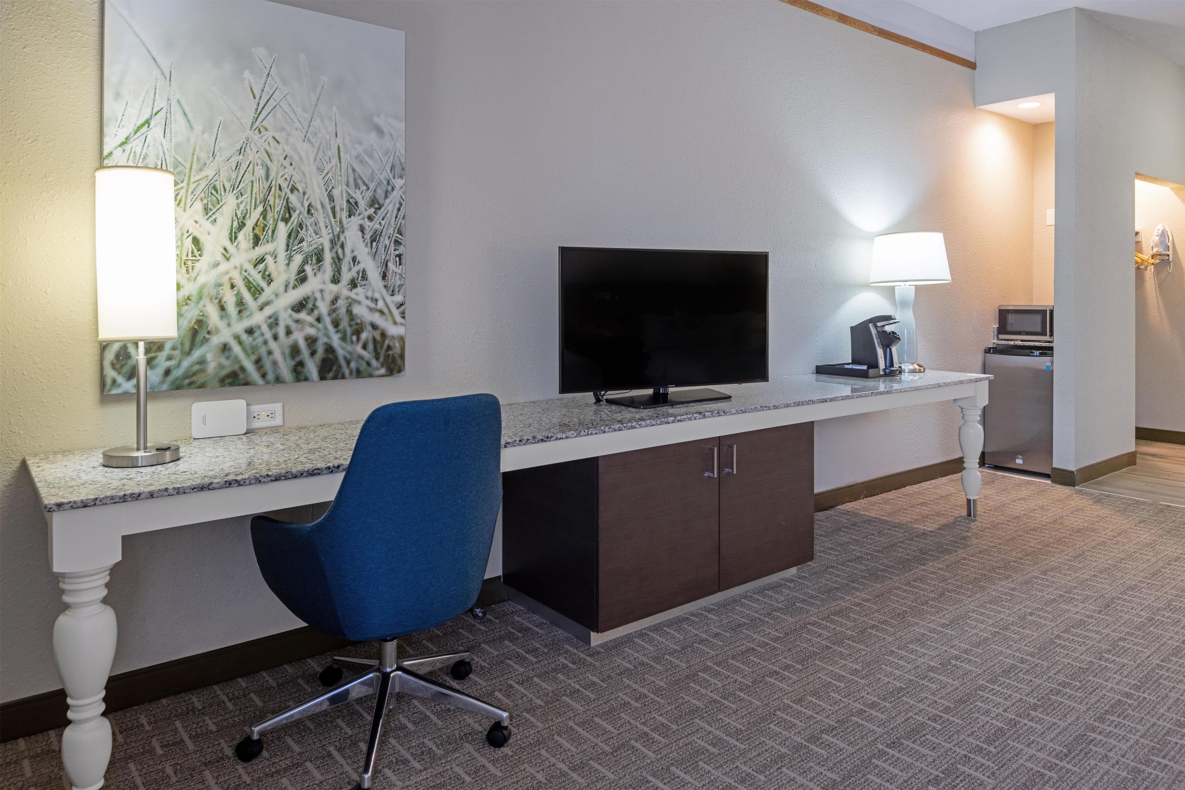 A hotel room with a desk, chair, television, lamp, and a painting on the wall.