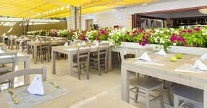 A restaurant with multiple tables, chairs, and a yellow canopy. - Insotel Cala Mandía All Inclusive Resort & Spa (Manacor)
