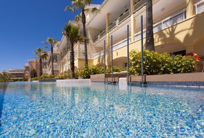 A swimming pool with clear blue water, surrounded by palm trees and a multi-story hotel building with balconies. - Insotel Cala Mandía All Inclusive Resort & Spa (Manacor)