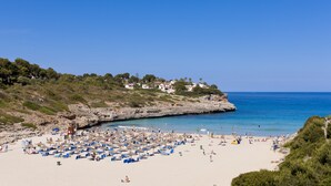 Una playa con numerosas tumbonas y sombrillas, un litoral rocoso y casas en una ladera.