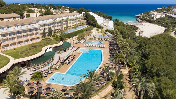 Un resort con una amplia piscina, varias zonas de descanso y una playa.