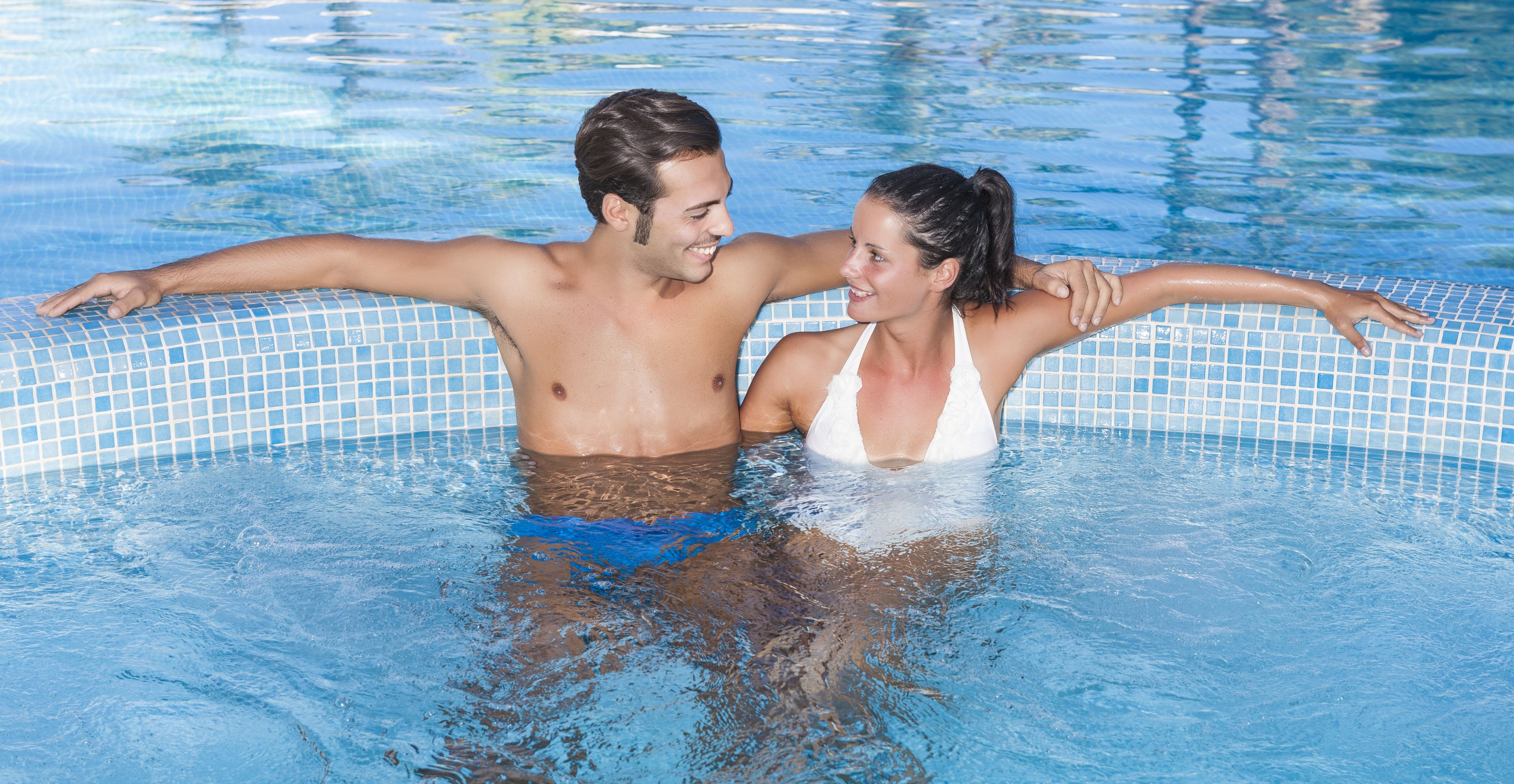 Una pareja en una piscina con bordes de azulejos.