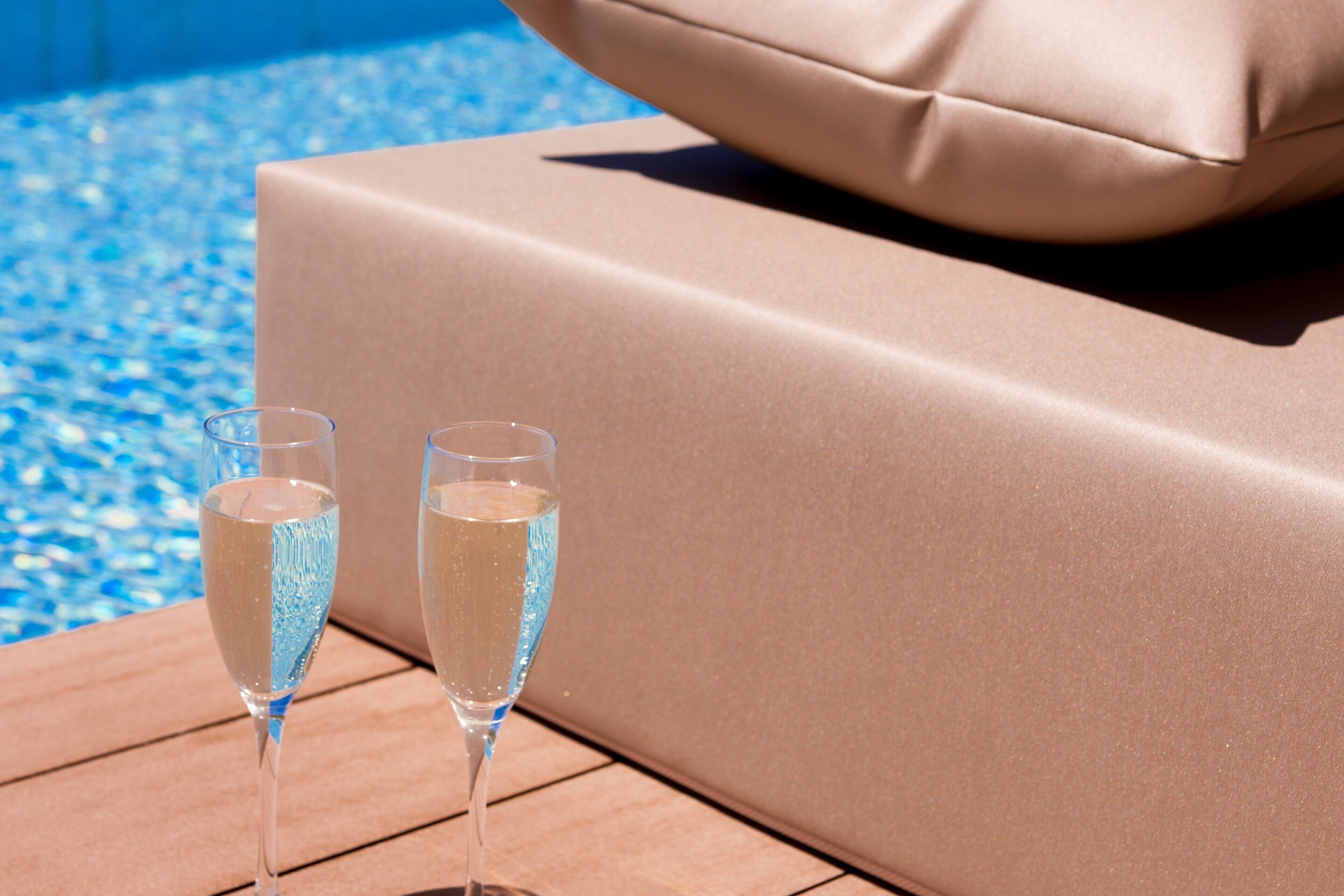 To champagneglas på et træbord ved en poollounge med en beige pude.