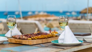 Una mesa con una tabla de fiambres y verduras, dos servilletas blancas y una copa de vino blanco.