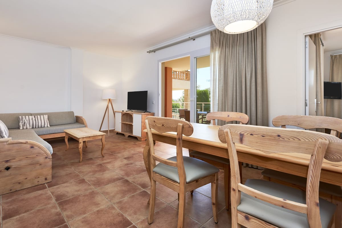 A living room with a sofa, wooden dining table, chairs, a TV, and a lamp.