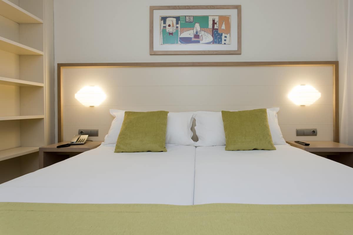 A hotel room with a large bed, two bedside lamps, a painting on the wall, and a telephone on the nightstand.