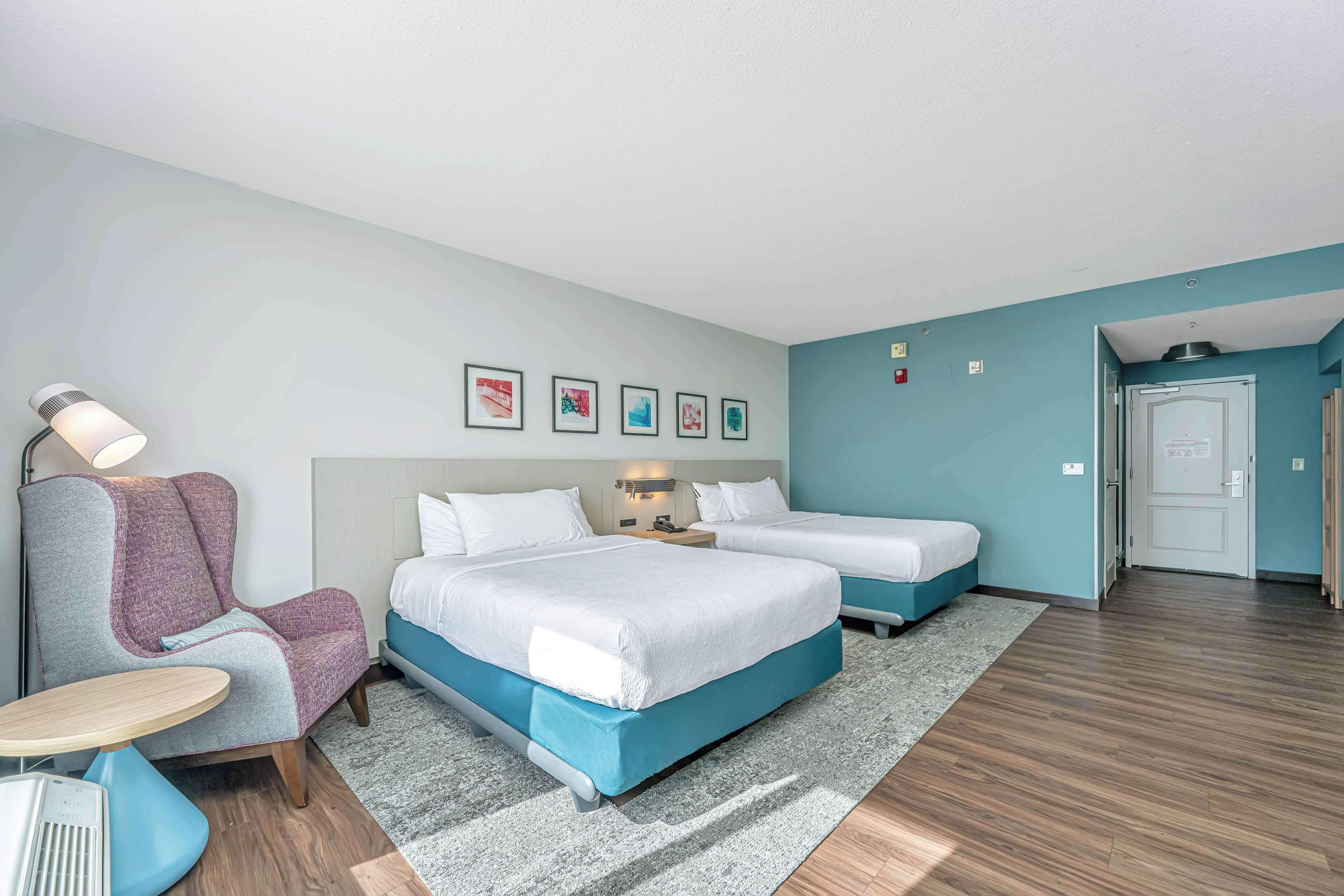 Une chambre d’hôtel avec deux lits, une chaise, une petite table et une table de chevet.
